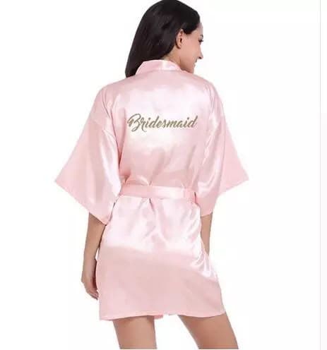 A blush satin robe with Bridesmaid embroidered in gold across the back