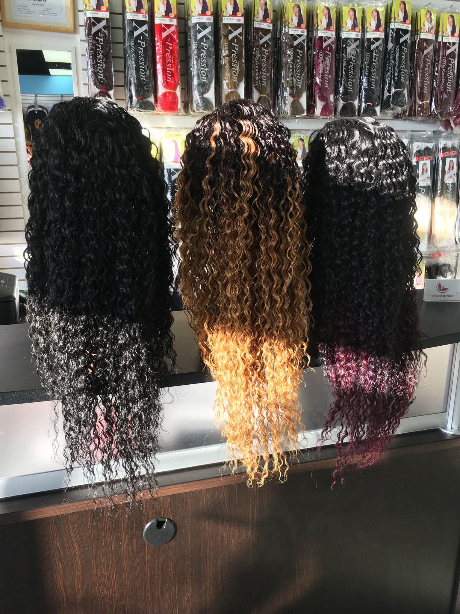 Three curly wig units in black, honey blonde and burgundy on the counter
